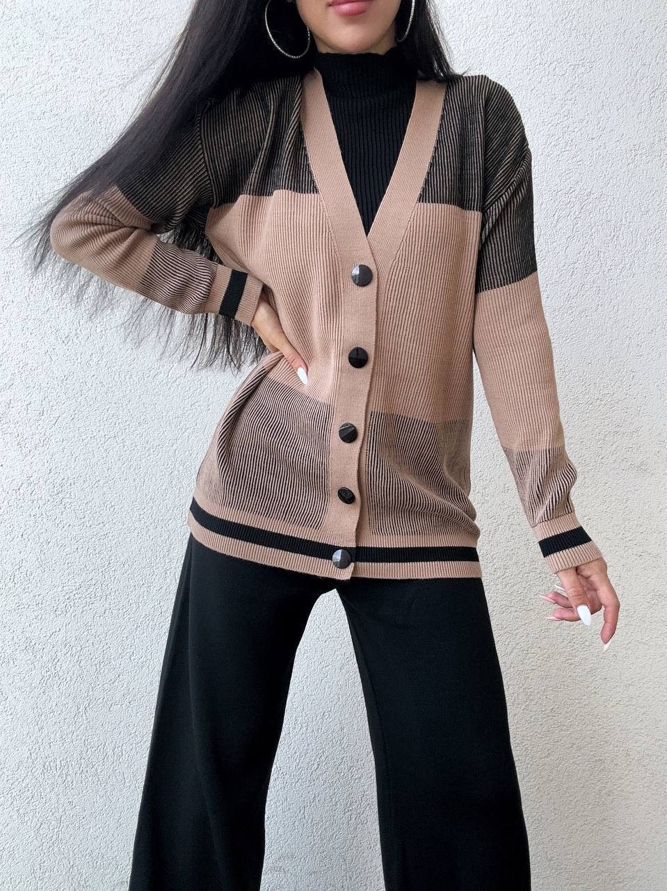 Person wearing a beige cardigan with black buttons against a white background