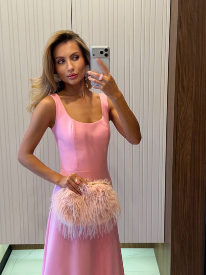 Woman in a pink dress holding a feathered clutch in front of a mirror.