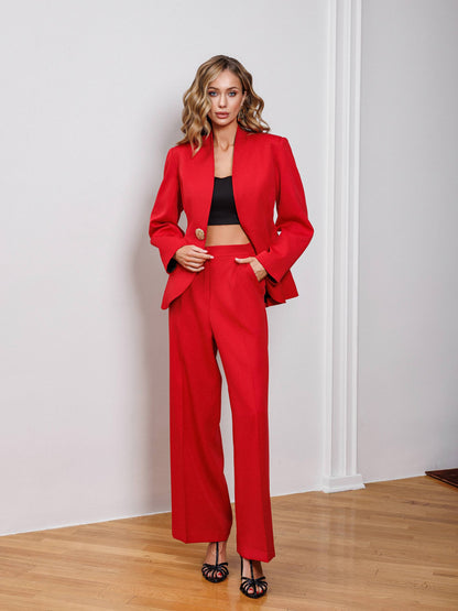 Woman wearing a red suit standing against a white wall.