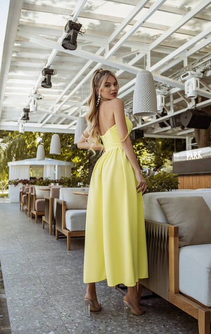 Woman in a yellow dress standing in an outdoor setting with white pergola and wooden furniture.