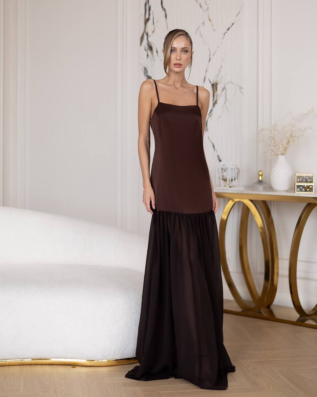 Woman wearing a brown slip dress in an elegant room with marble walls and a gold side table.