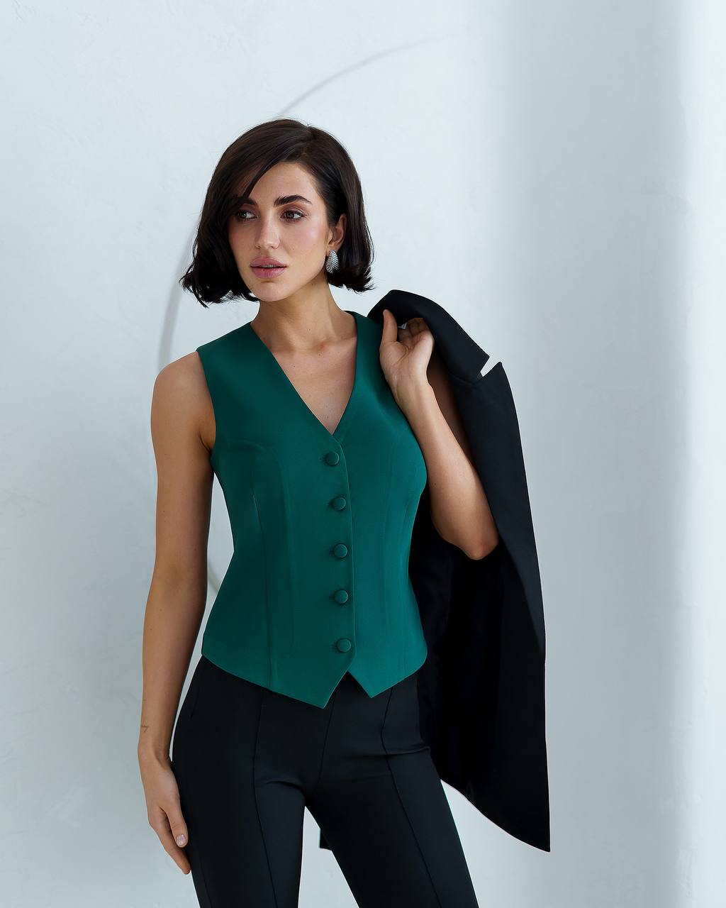 Woman wearing a green vest and black pants against a white background