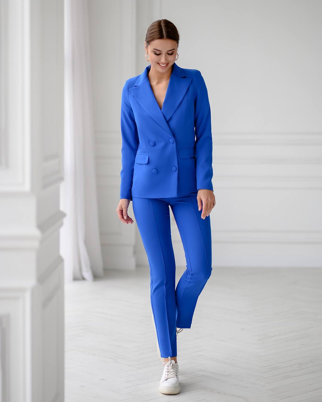 Woman wearing a blue suit with white sneakers in a minimalistic setting