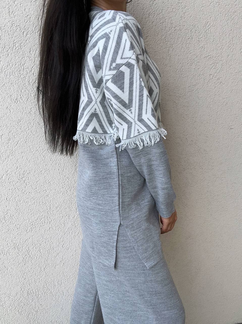 Person wearing a gray and white patterned top with a plain background