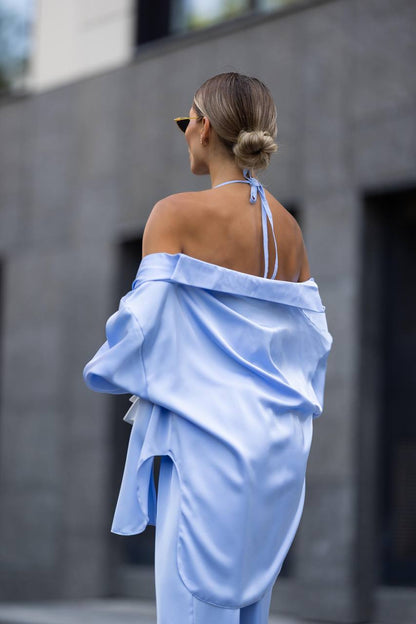 Woman wearing a light blue off-shoulder outfit against a gray wall.