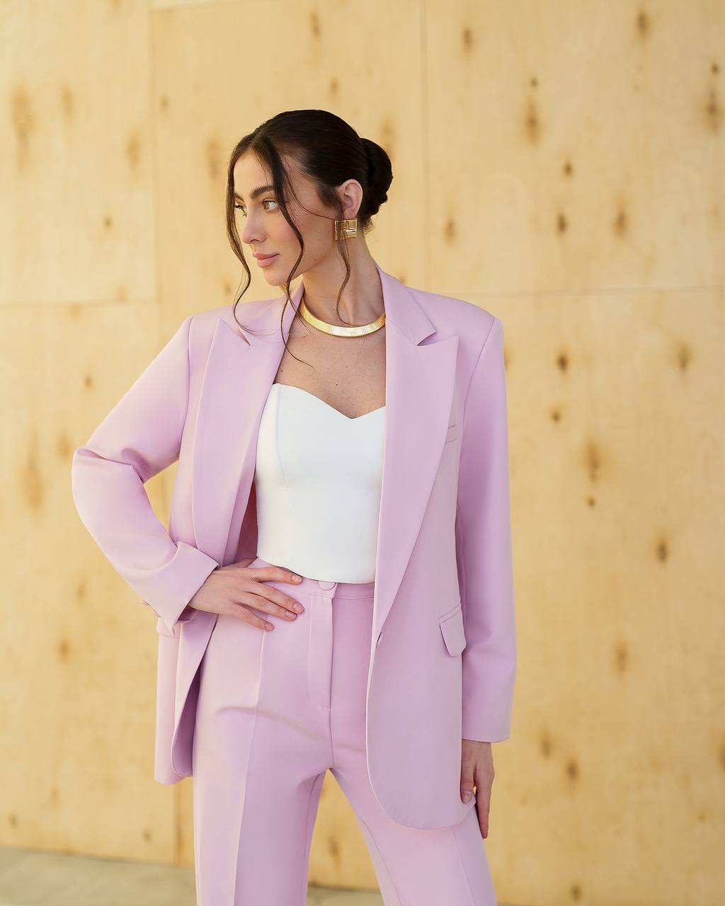 Woman wearing a light purple suit with a white top against a wooden background