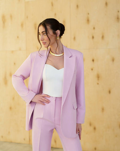 Woman wearing a light purple suit with a white top against a wooden background