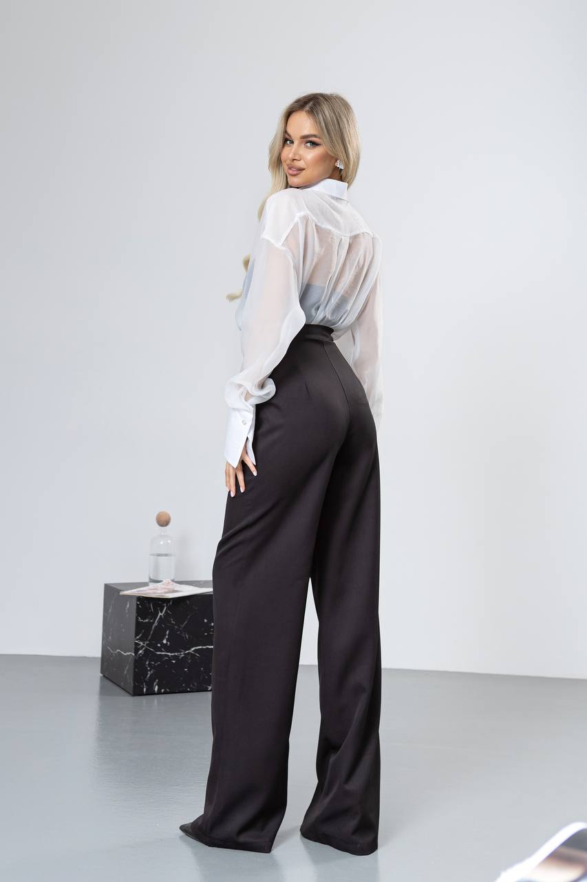 Woman wearing a white blouse and black pants in a minimalistic setting