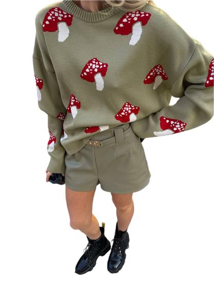 Person wearing a green sweater with red mushroom patterns and beige shorts on a white background