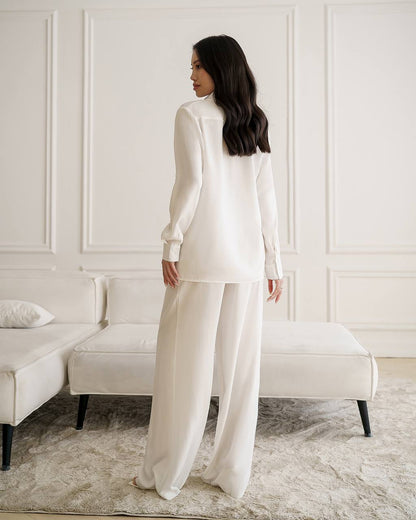 Woman in a white outfit standing in a room with white walls and furniture.