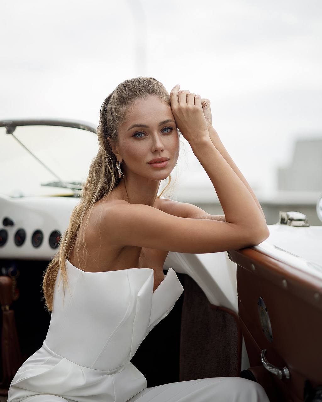 Woman in a white dress sitting inside a vintage car with a blurred background