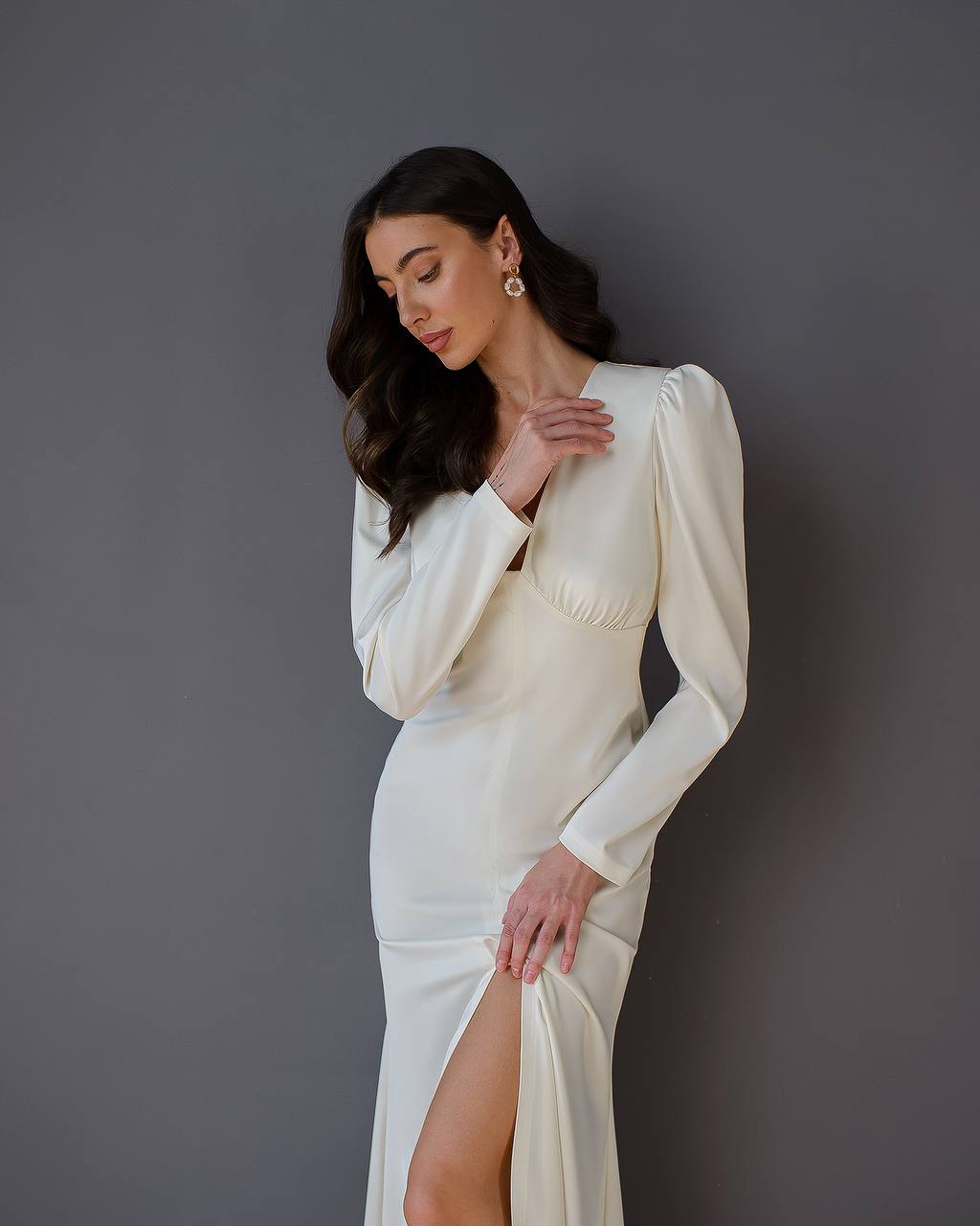 Woman wearing a white dress with long sleeves against a gray background