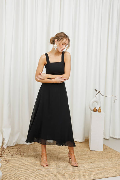 Woman wearing a black dress standing in front of white curtains