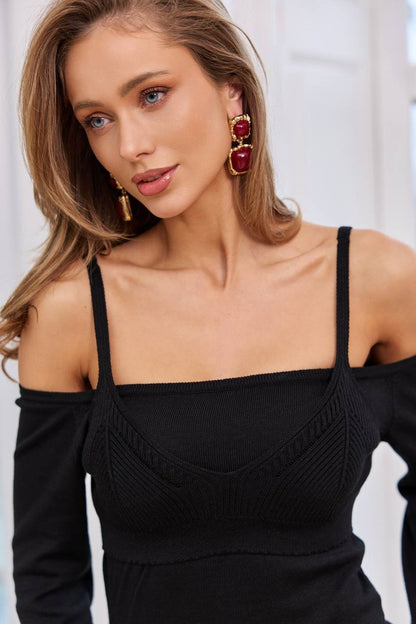 Woman wearing a black off-shoulder top with red earrings against a white background