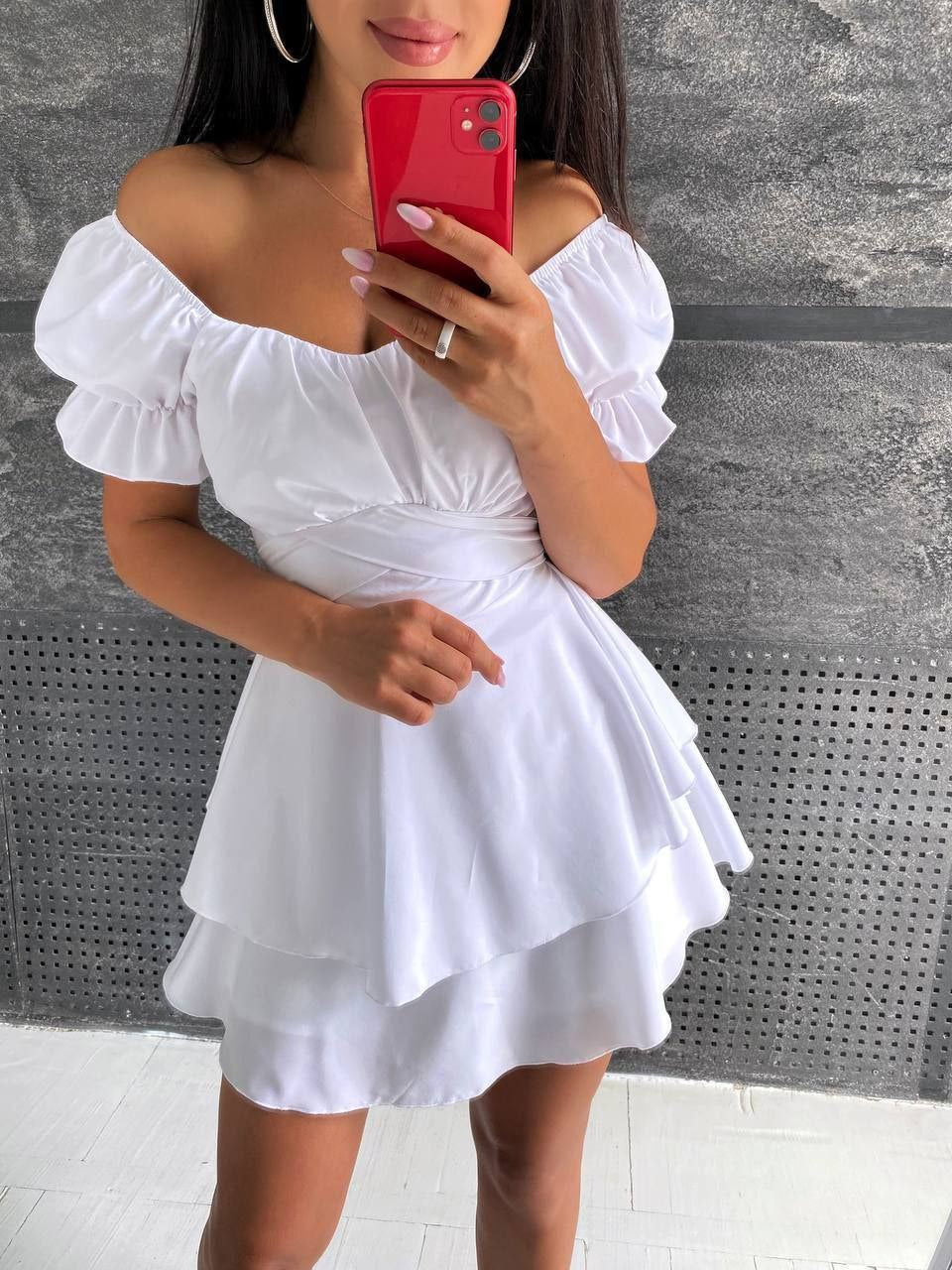 Woman wearing a white off-shoulder dress taking a mirror selfie.