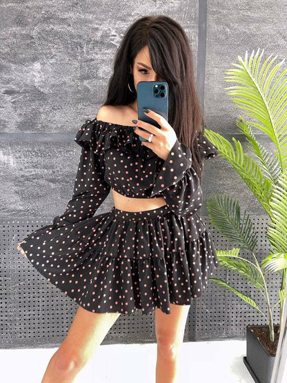 Woman taking a mirror selfie wearing a black polka dot dress against a gray wall with a plant.