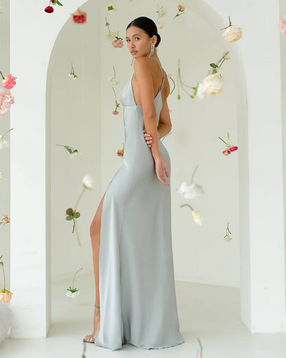 Woman in a light blue gown with a high slit standing against a floral decorated wall.