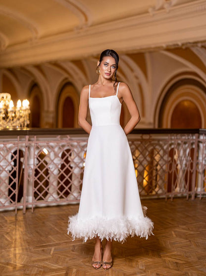 Woman in a white dress with feather details standing in an elegant indoor setting.