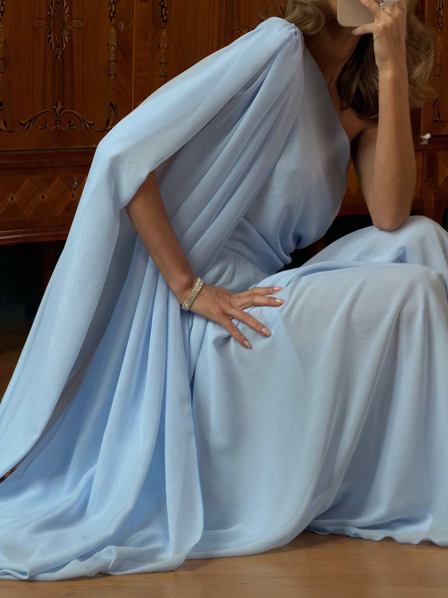 Woman in a flowing light blue dress sitting on a wooden floor.