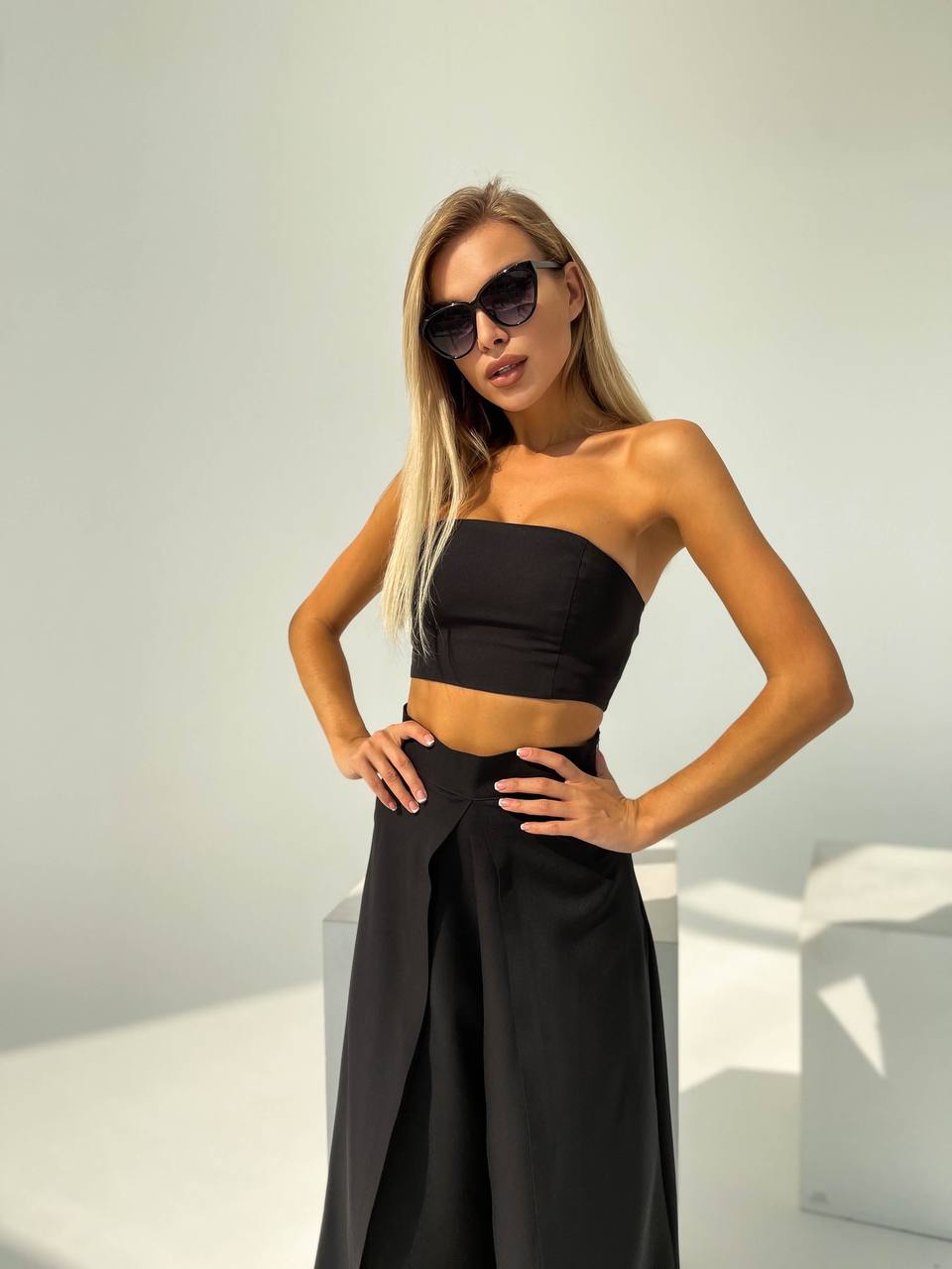Woman wearing a black strapless top and skirt with sunglasses against a white background