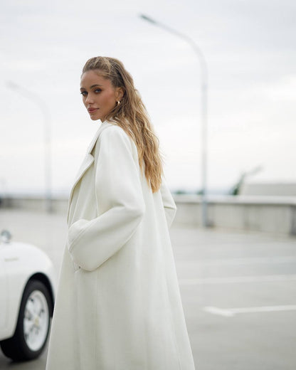 Woman wearing a white coat standing in an urban setting with blurred background