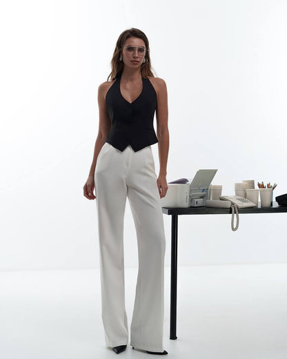 Woman in black top and white pants standing next to a desk with office supplies on a white background