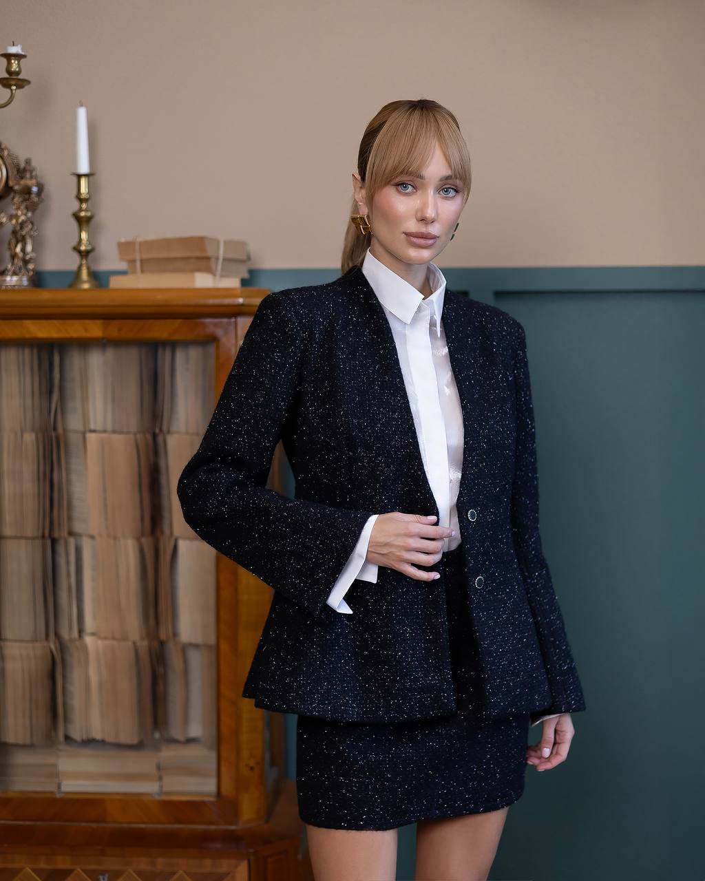 Woman wearing a dark blazer and skirt set with a white shirt indoors.