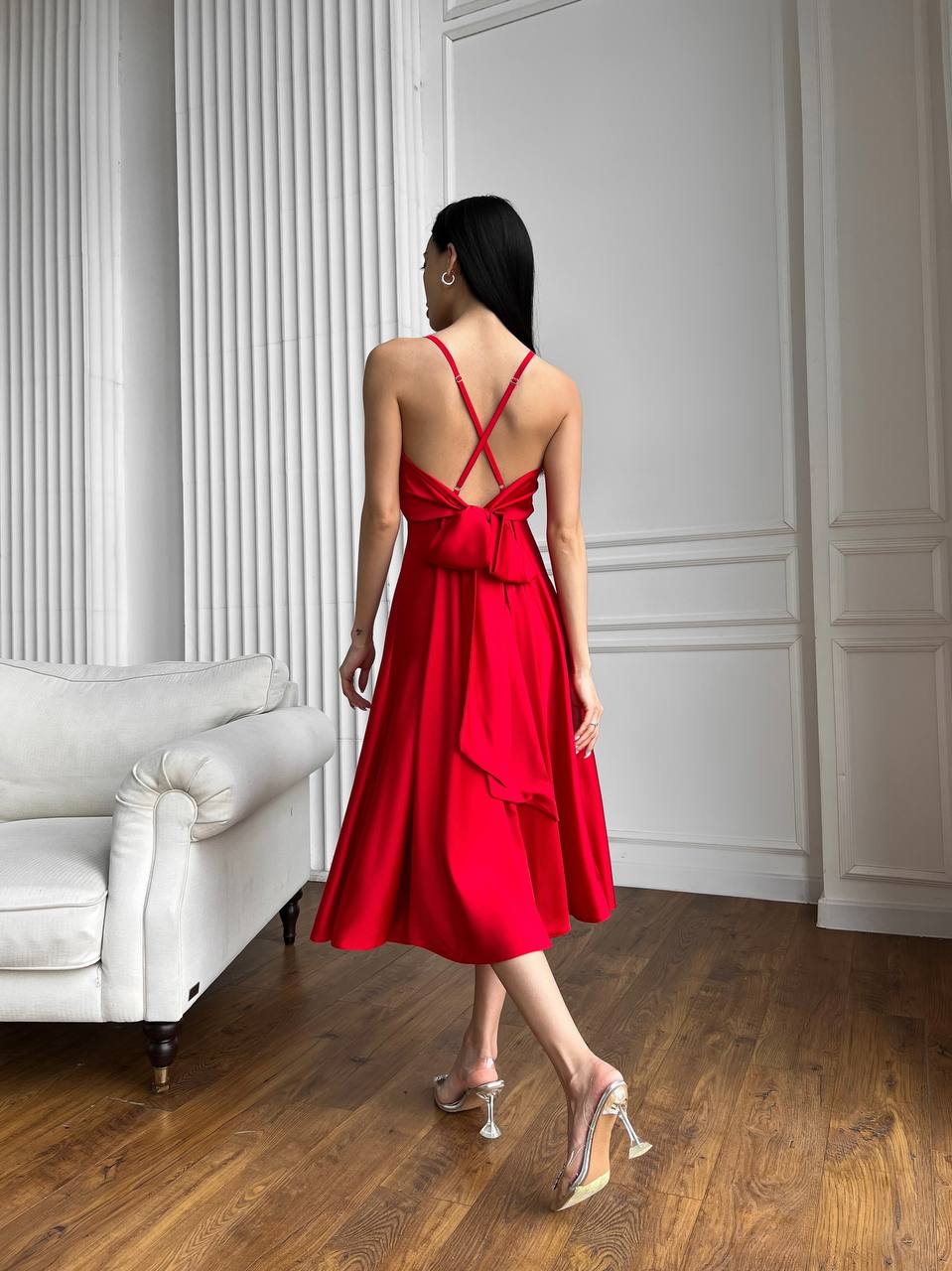 Woman in a red dress standing in a room with white walls and a white sofa.