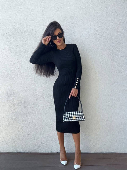 Woman in a black dress holding a checkered handbag against a white wall