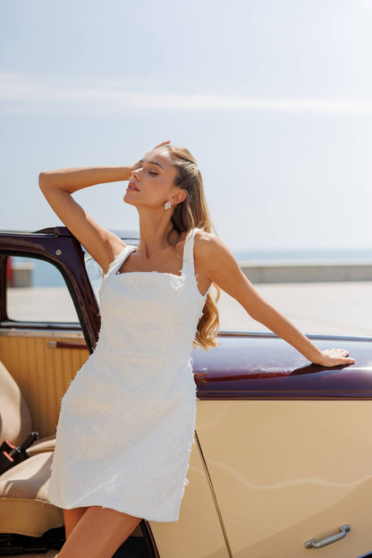 Woman in a white dress standing next to a vintage car with a clear sky background