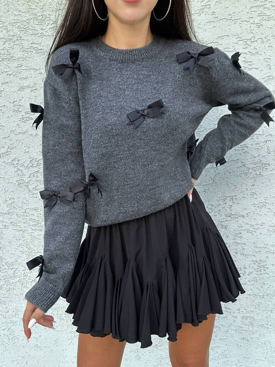 Gray sweater with black bows and a black skirt on a textured light gray background