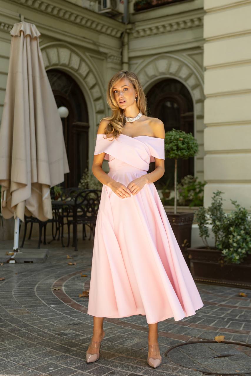 Woman in a pink off-shoulder dress standing outdoors near a building entrance.