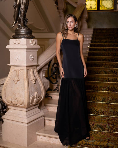 Woman in a black dress standing on a grand staircase with ornate railings.