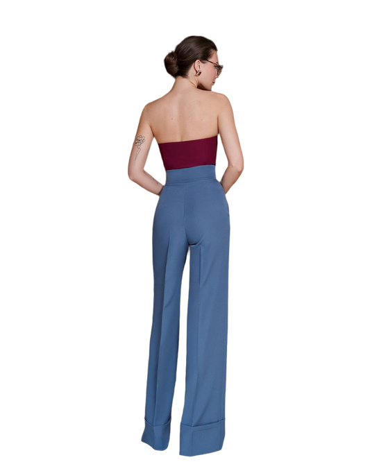Woman wearing a strapless burgundy top and high-waisted blue pants on a white background