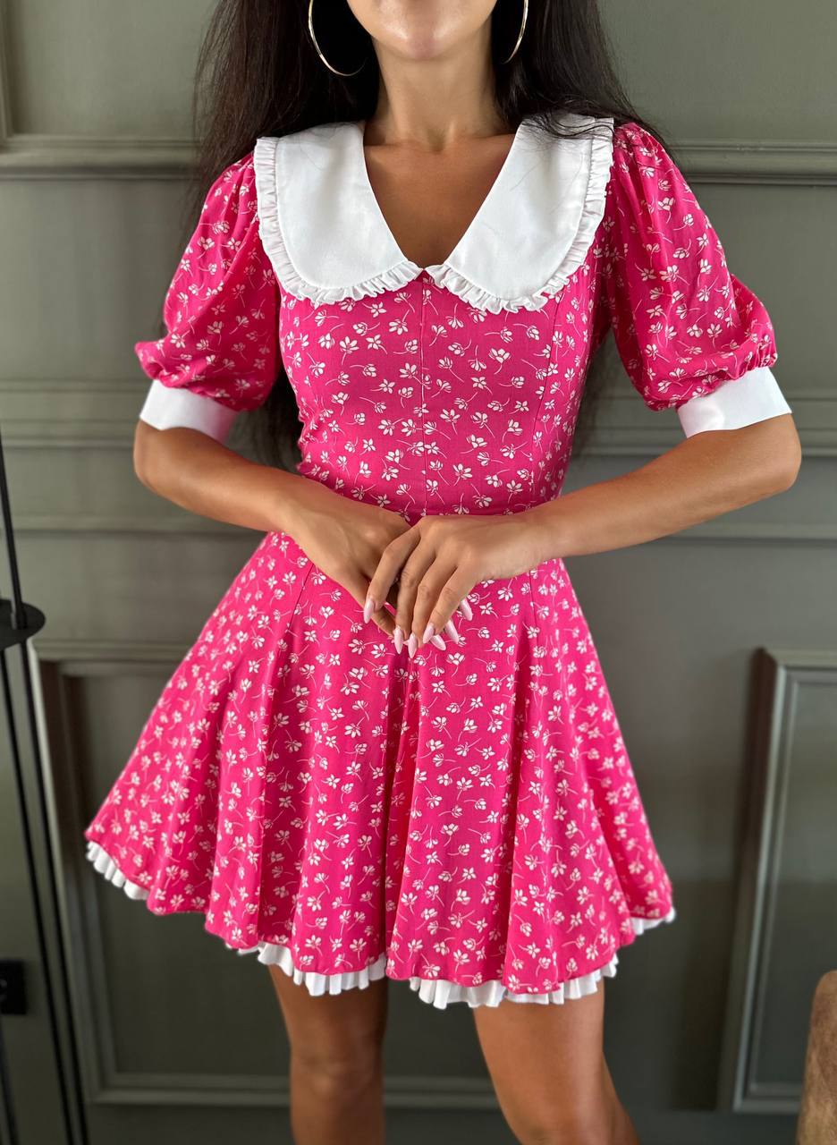 Woman wearing a pink dress with white floral pattern and collar against a neutral background
