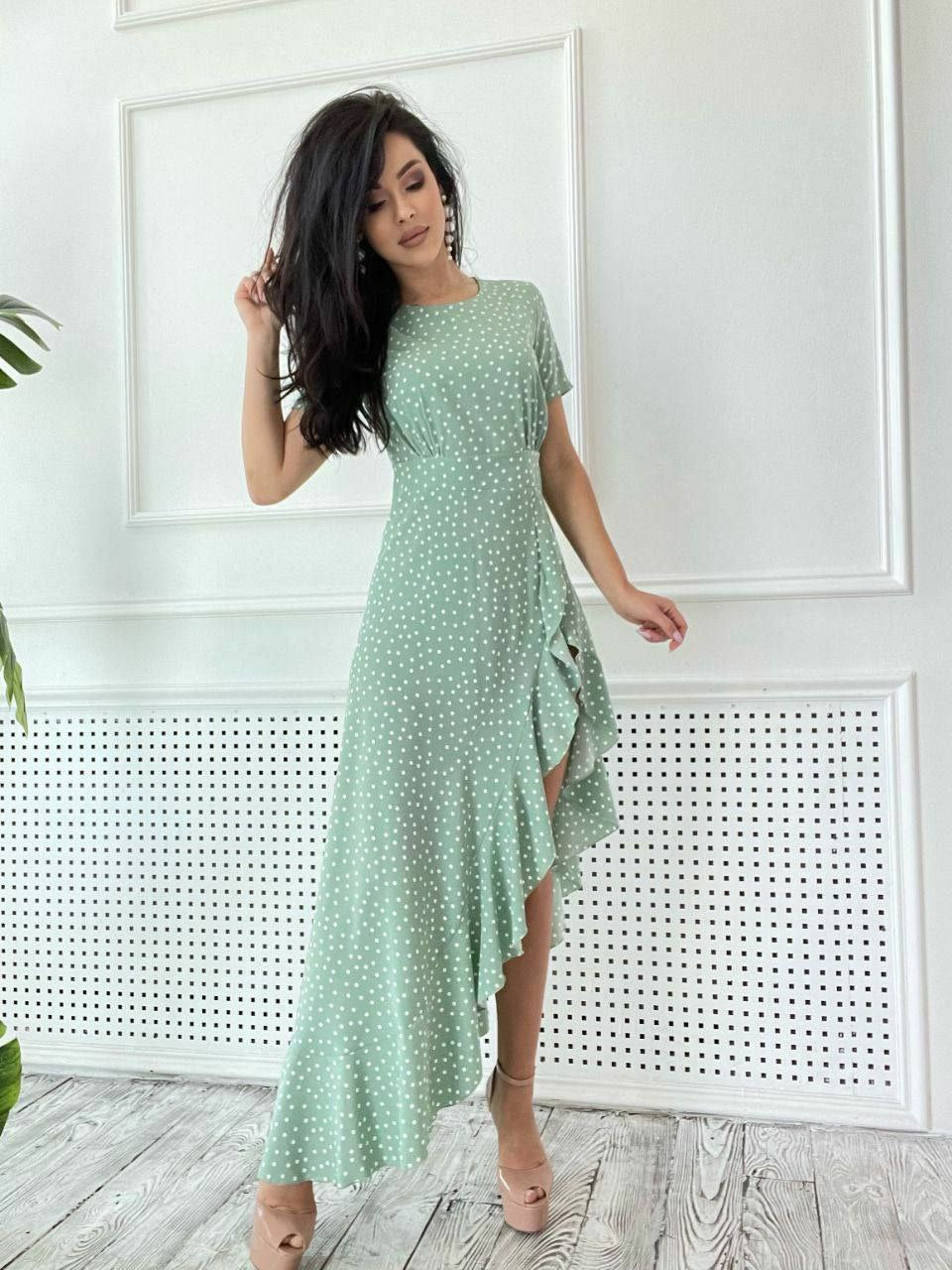Woman wearing a green dress with white polka dots in a minimalistic room.