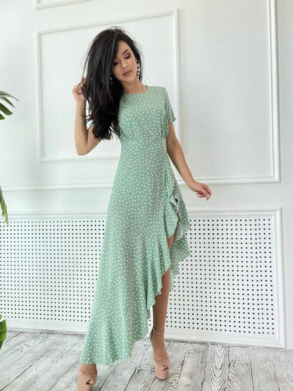 Woman wearing a green dress with white polka dots in a minimalistic room.