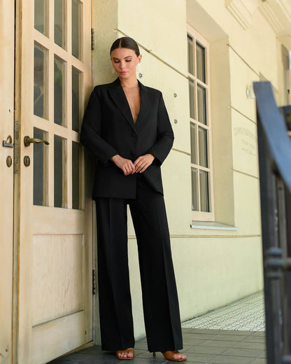 Woman in a black suit standing in front of a building entrance.