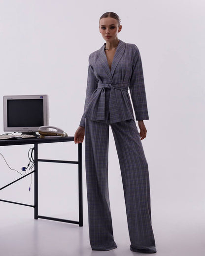 Woman in a gray checkered suit standing next to a desk with a computer monitor on a white background
