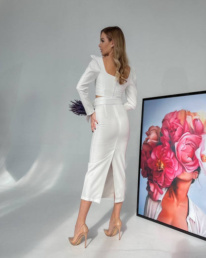 Woman in a white outfit standing next to a framed artwork of flowers.