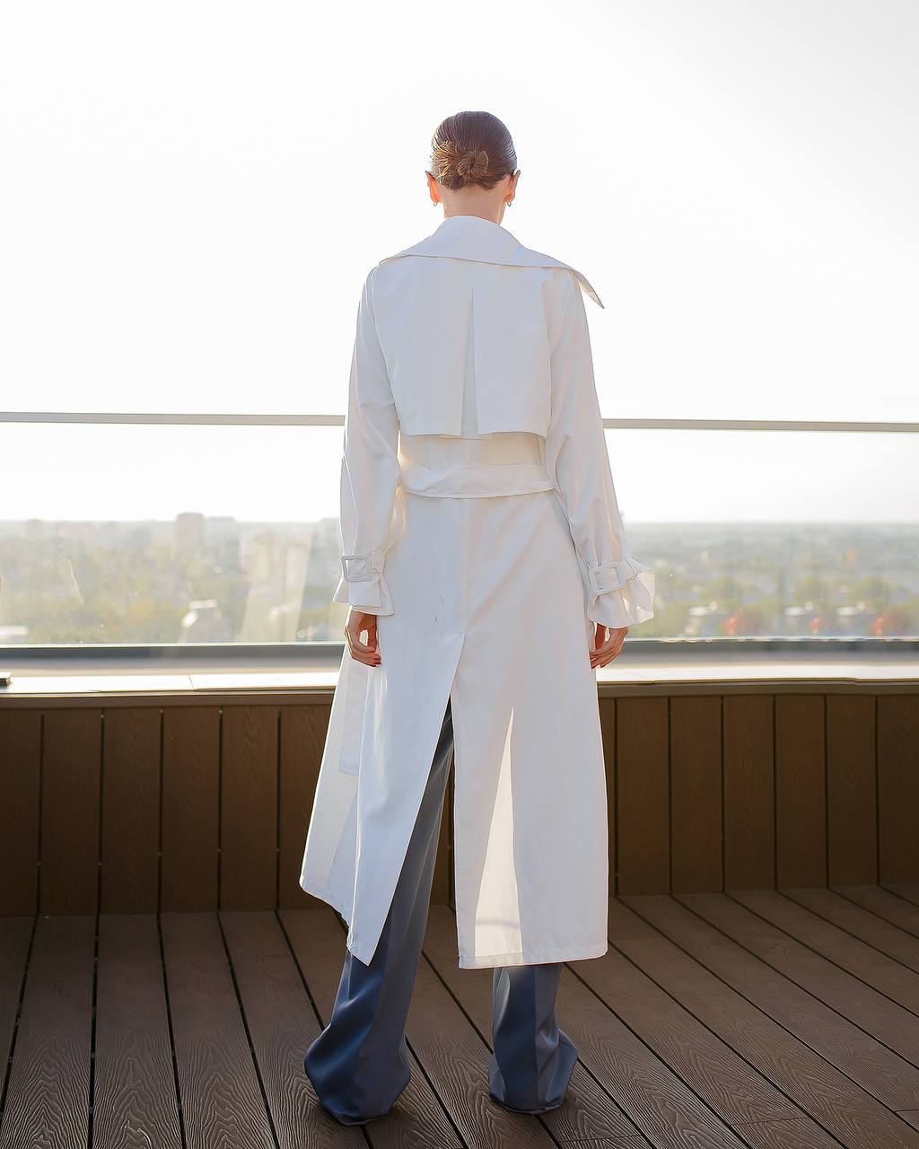 Person wearing a long white coat on a wooden deck with a cityscape in the background