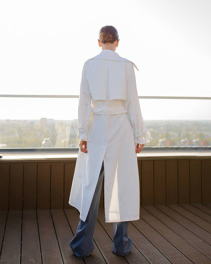 Person wearing a long white coat on a wooden deck with a cityscape in the background