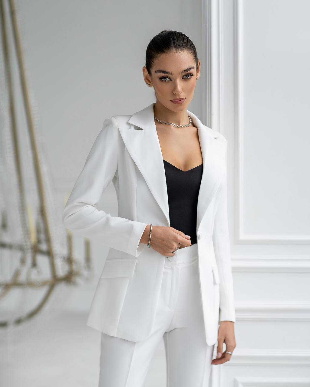 Woman wearing a white suit standing in a minimalistic room.