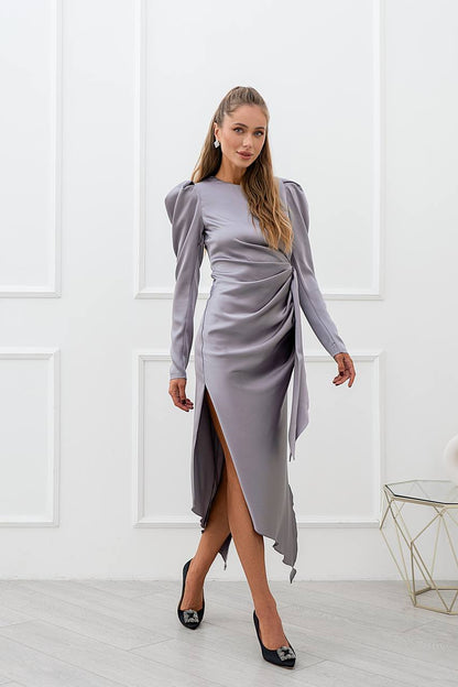 Woman wearing a gray dress with long sleeves and a slit skirt in a minimalistic room.
