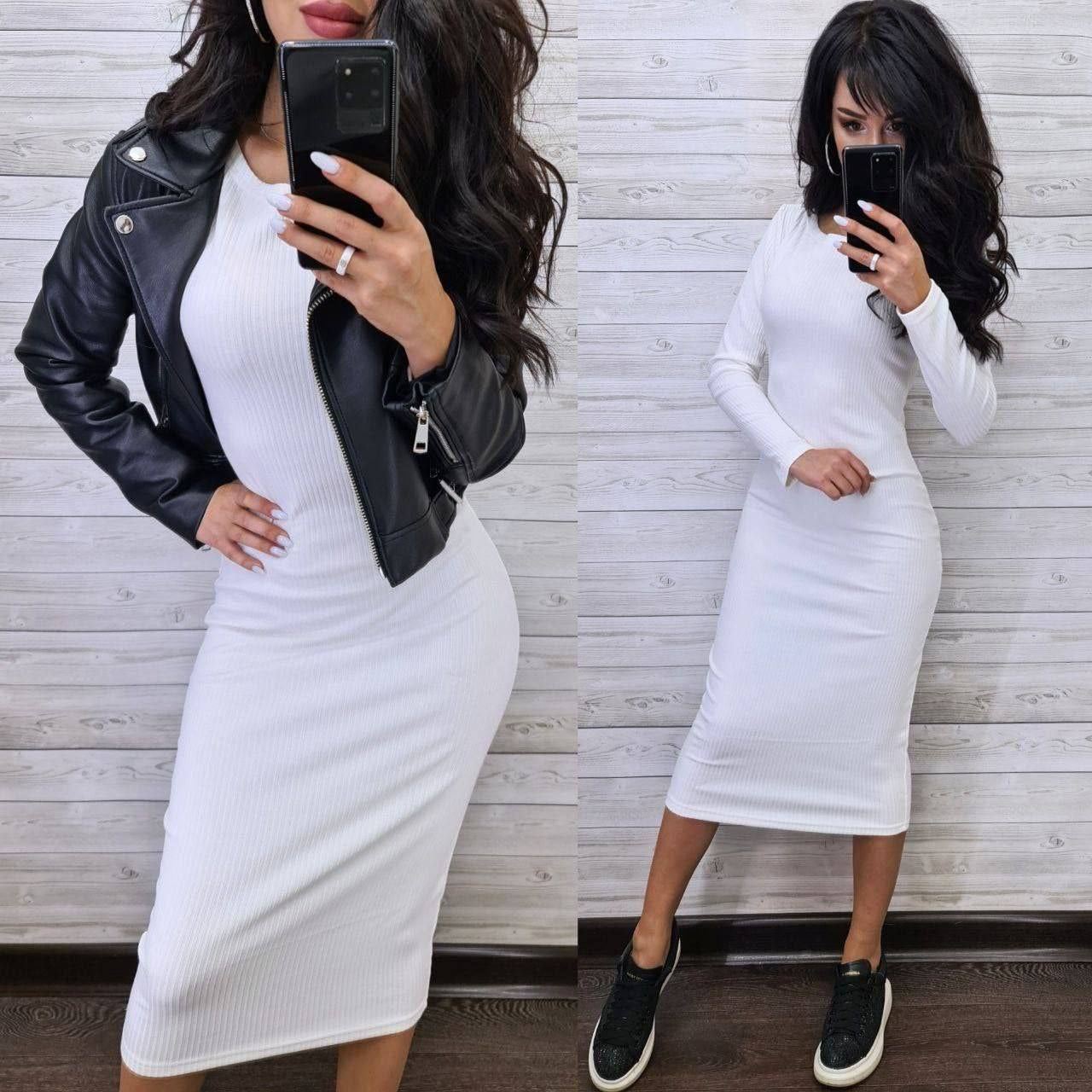 Woman wearing a white dress with a black leather jacket and black shoes, taking a mirror selfie.