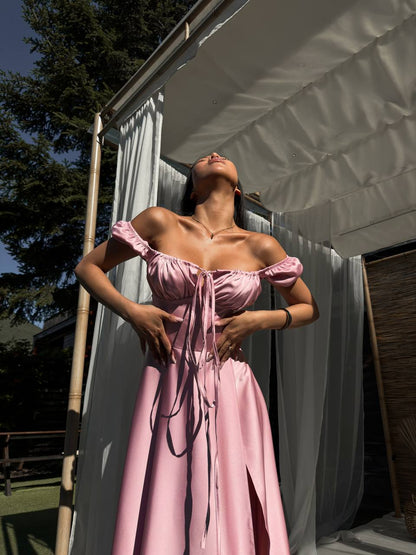 Woman in a pink dress standing outdoors with trees and a building in the background