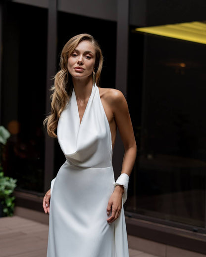 Woman wearing a white halter neck dress standing outdoors.