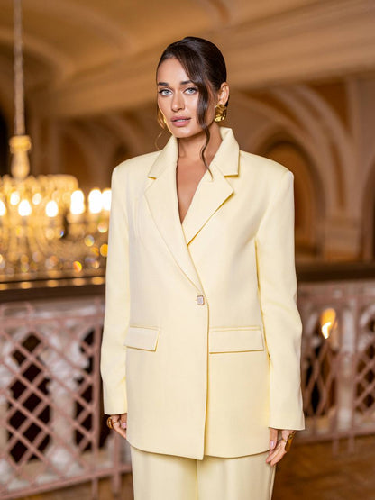 Woman in a light yellow suit standing in an elegant interior setting with chandeliers.