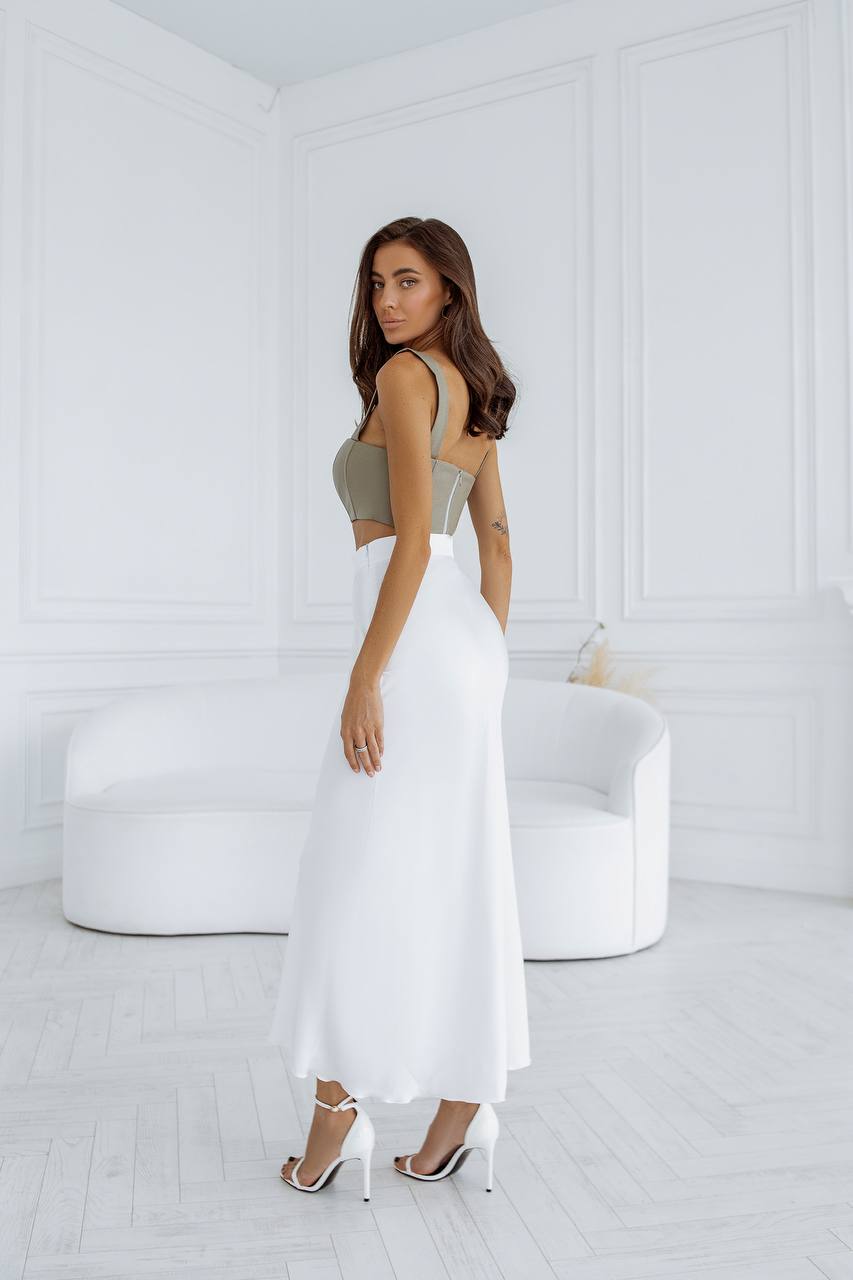 Woman in a white dress standing in a minimalistic room with white walls and furniture.