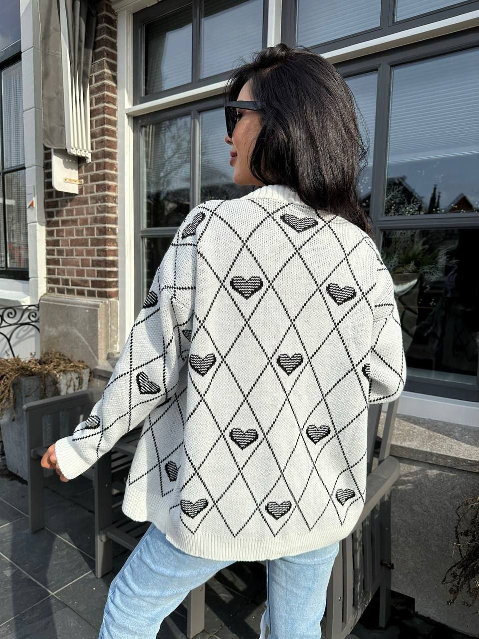 Person wearing a white cardigan with black heart patterns outdoors.